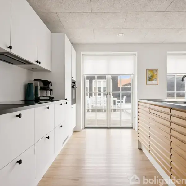 Et gult hus med rødt tegltag står på en brolagt indkørsel ved siden af en vej. Baggrunden viser flere lignende huse i et boligområde.