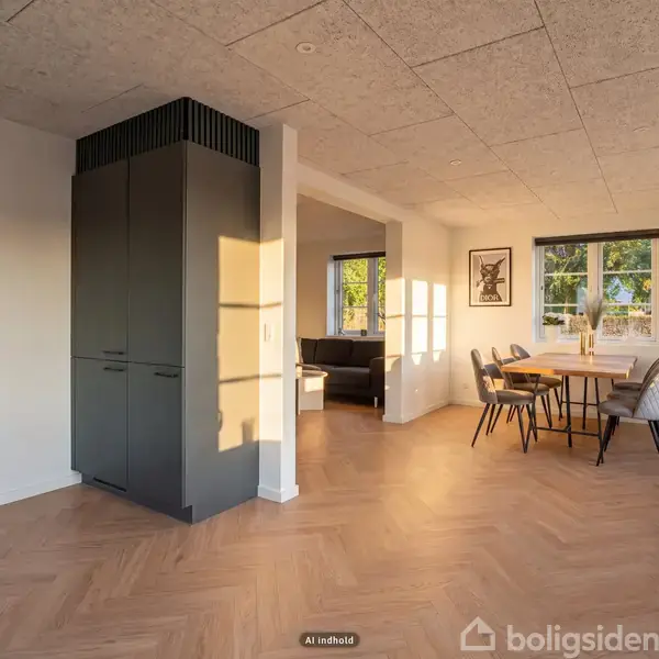Et moderne køkken med mørkegrå skabe er central. Et spisebord med stole står ved vinduet. Sollys strømmer ind i rummet med parketgulv og minimalistisk indretning.