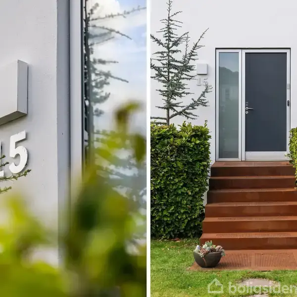 En moderne hvid husfacade med nummeret "15" og en dør med glasrude. Trætrapper fører op til døren, omgivet af velplejet hæk og en græsplæne med krukkeplanter.