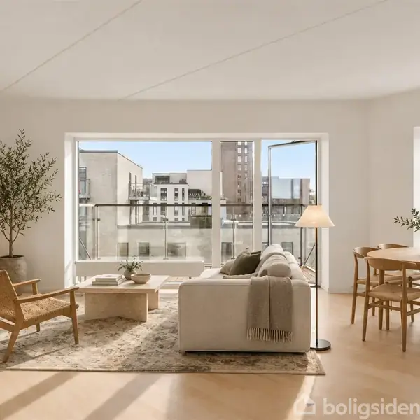 En lys stue med sofa og lænestol omkring et kaffebord, inaktive, flankeret af en skænk med lampe og plante. Store vinduer viser byudsigt og giver rigeligt lys.