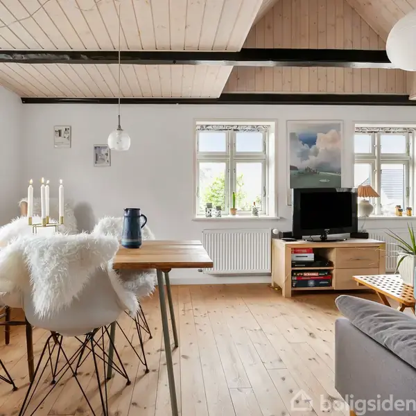 En lys stue med træloft og gulv. Et spisebord med stearinlys og stole er til venstre. Til højre er en sofa og et tv ved vinduer. Afslappet atmosfære.