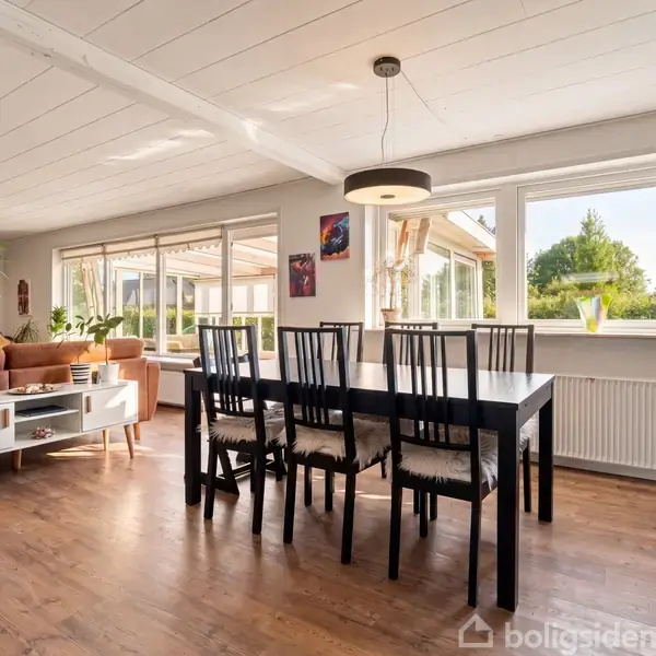 Et moderne spisebord med seks stole står i en lys spisestue. Store vinduer giver udsigt til en grøn have, og rummet er dekoreret med vægkunst og planter.