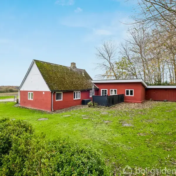 Rødt hus står stille på en grøn græsplæne omgivet af træer og buske under en blå himmel.