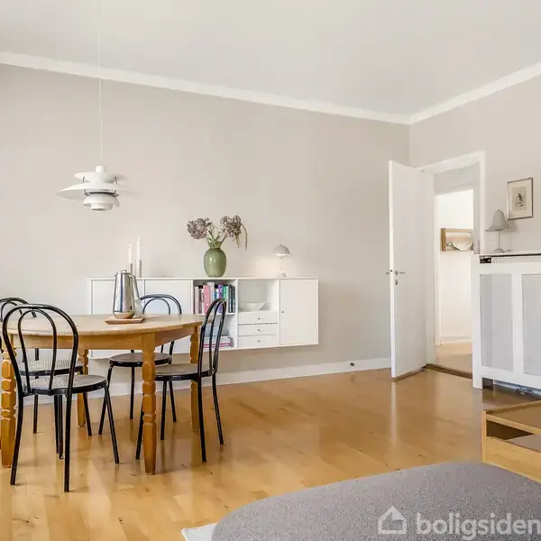 Et rundt spisebord med stole står i et lyst rum med trægulv. En væghængt hylde har vaser. Der er dør til et tilstødende rum; moderne og minimalistisk indretning.