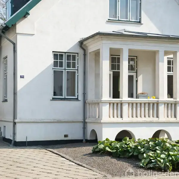 Hvid villa med trappetrin til veranda, omgivet af fliser og grønne planter. Verandaen har søjler og store vinduer. Adressenummer "14" ses ved indgangen.
