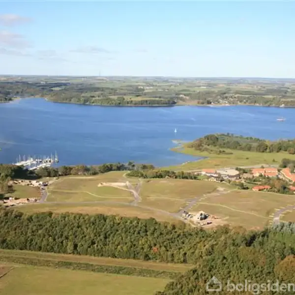 En stor sø med omkringliggende landskab, herunder marker, skove og en havn med både. Landskabet strækker sig mod horisonten under en blå himmel med enkelte skyer.