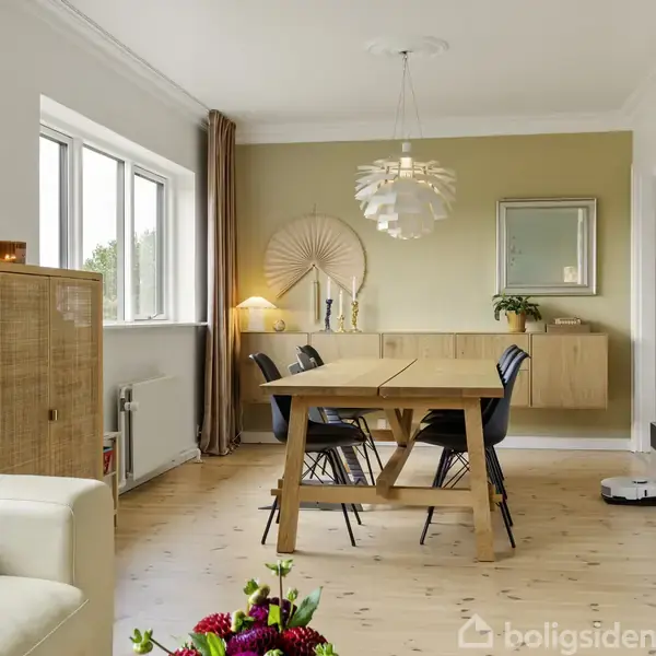 Et spisestueområde med et træbord og fire stole. Bagved hænger en kunstnerisk lampe fra loftet. På væggene findes kunstværker, et spejl og et skab.
