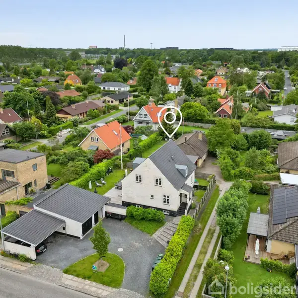 Et hvidt murstenshus med sort tag har en stor terrasse med havemøbler og grill. Terrassen har udsigt over en velplejet græsplæne.