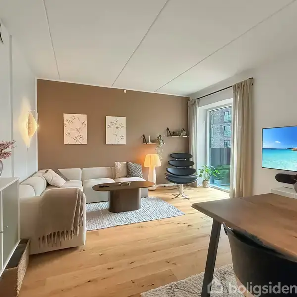 En stue med sofa og sofabord på et tæppe, vægkunst på en brun væg, lænestol ved glasdør, og et fladskærms-tv på møbel. Hyggelig, moderne indretning.