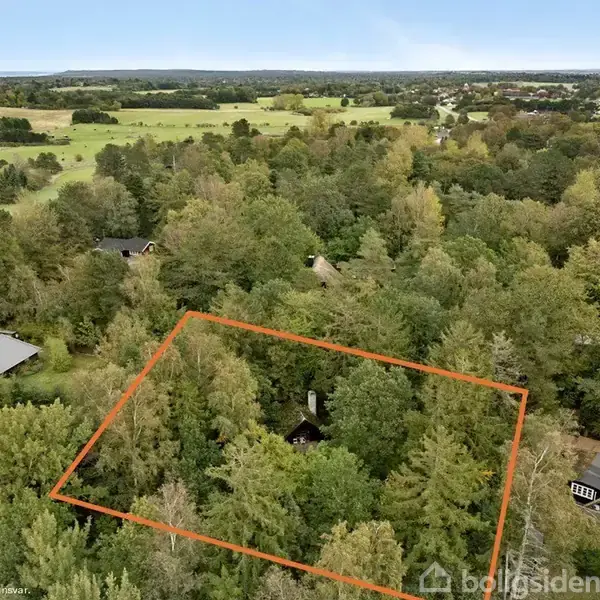 Et område omgivet af tæt skov markeret med en rød linje. I midten ses et lille hus omkranset af træer. Omkringliggende landskab består af marker og spredte huse.