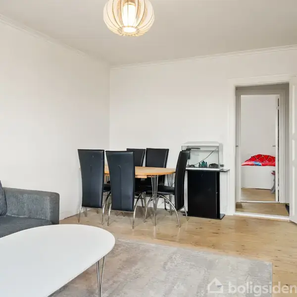 Rød murstensbygning med tre etager, mange vinduer og fladt tag. Flere biler er parkeret foran. Omgivet af et beboelseskvarter med huse og træer.