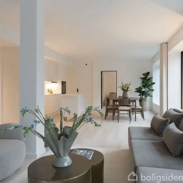 Moderne stue indeholder en grå sofa med puder, to runde, lyse lænestole, og et sofabord med blomster i vase. I baggrunden ses spisebord med stole, omgivet af store vinduer og planter.