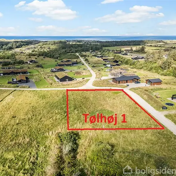 Grønt græsareal med rød markeringsramme omkring, der angiver en grund med teksten "Tølhøj 1". Området er i nærheden af moderne boliger og veje, med skov og hav i horisonten.