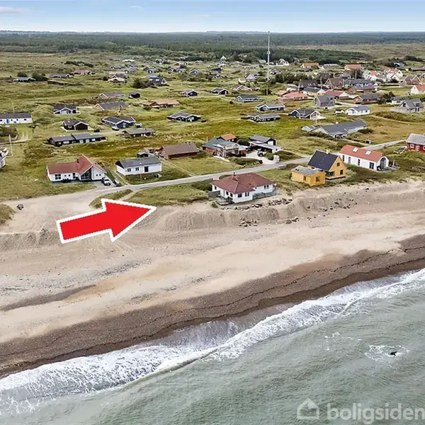 En rød pil peger på et hus langs en kystlinje, omgivet af flere huse. Forgrund viser en strand og hav, mens baggrunden består af åbne grønne områder.