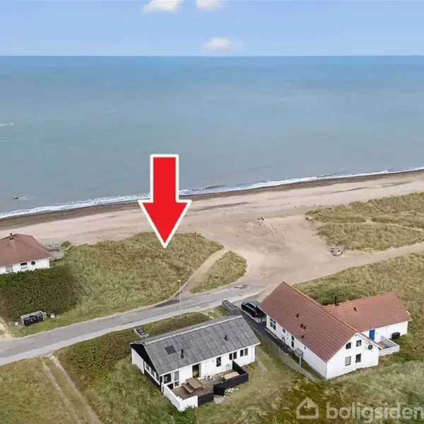 Et rødt pil peger ned mod en kystnær grund ved havet. Omgivet af strand, græs og huse, symboliserer pilen muligvis et interessant område.