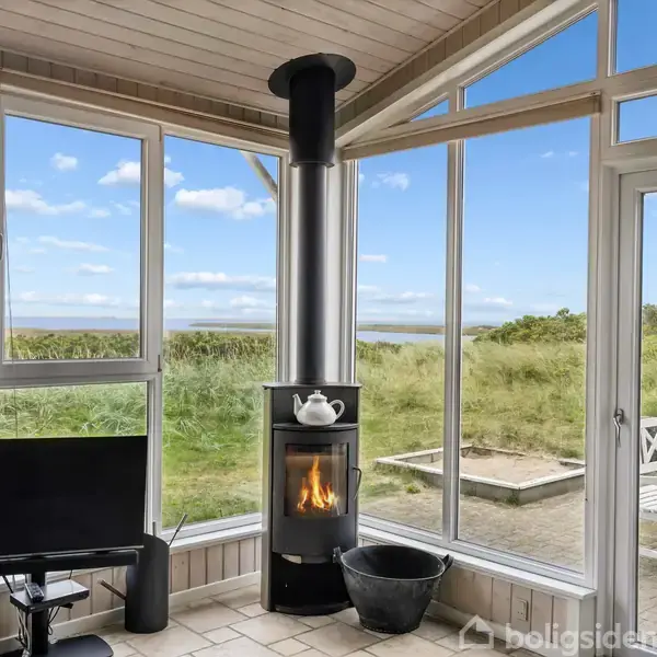 Pejs med ild ved siden af en lille tv-skærm i en glasindrammet stue. Udenfor ses en terrasse med havemøbler og grill, omgivet af en grøn eng og blå himmel.