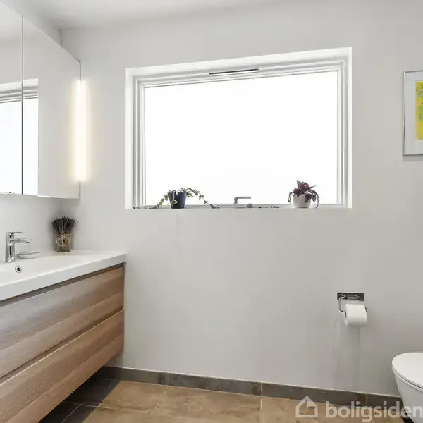 Et boligområde med mange huse, en rød pil peger mod ét specifikt hus. Området ligger nær kysten, omgivet af marker og veje.