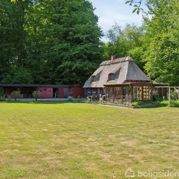 Hus med stråtag står ved siden af en stor plæne. Ved siden af huset er der en rød bygning og træer omslutter området, hvilket skaber en skovbevokset atmosfære.