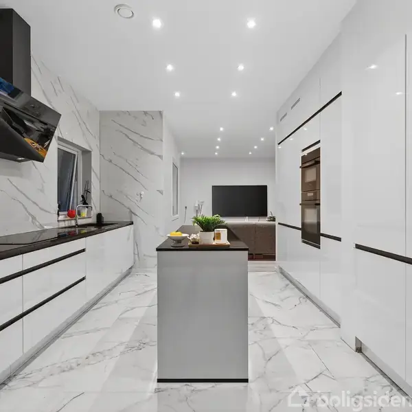 Et moderne køkken med hvide højglansskabe og en mørk bordplade, står i et marmorbeklædt rum med spots i loftet. Midt i rummet er en køkkenø med planter og madvarer.