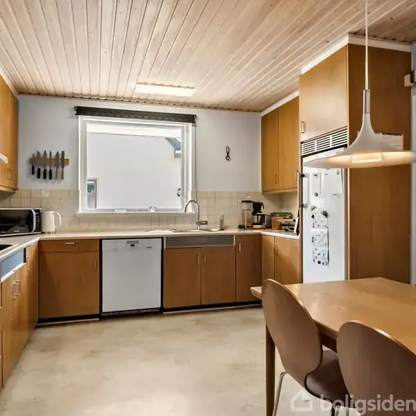 Køkken med træbordplade opstillet i vinkel, omgivet af skabe og skuffer. Et bord med stole står centralt, og et vindue samt moderne apparater fuldender det lyse, funktionelle rum.