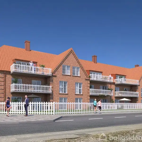 Et rødt murstensbyggeri med flere altaner står i solskin. Foran bygningen er der en fortov med gående mennesker og en bil på vejen.