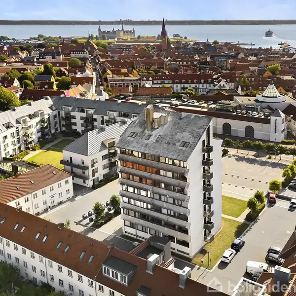 En lys stue med moderne møbler, hvor en mørkeblå stol står foran en beige sofa og sofabord, omgivet af planter. Store vinduer viser en altan og udsigt til havet. Tekst: "Lavet med AI".