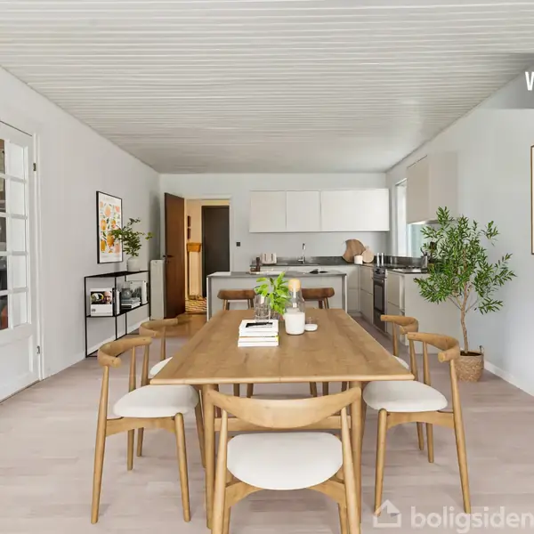 Spisebord med seks stole står i et lyst køkken-alrum med trægulv. Bordet er dekoreret med bøger og grønne planter. Omkring er hvide skabe, vægkunst og grønne planter. Tekst: "VISUALISERING".