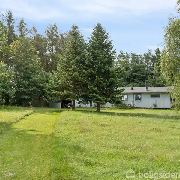 Huset står stille omkranset af høje træer og græsplæne, med en lille sti, der fører op til det.