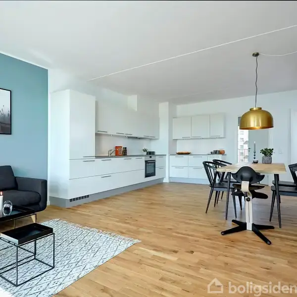 Sort sofa står i moderne stue med lyseblå væg, prydet af kunstværker. Trægulve forbinder spiseområde med sort bord og stole, mens et køkken med hvide skabe omfavner rummet.