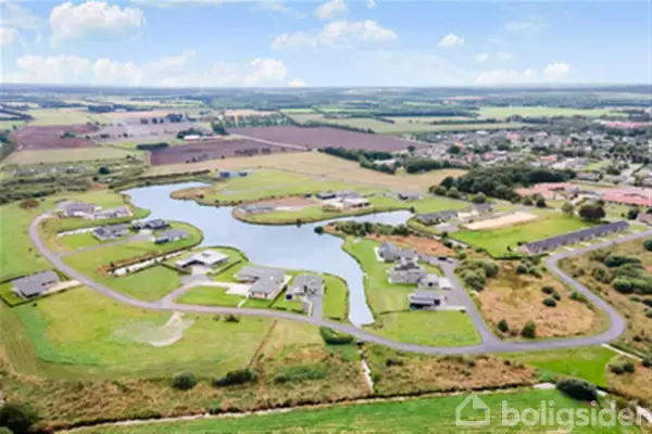 Boliger placeret langs snoede veje omkring en kunstig sø i et åbent, grønt landskab. Baggrunden består af marker og en by i horisonten.