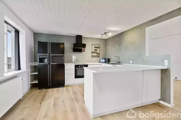 Køkken med sort køleskab, komfur og emhætte i moderne indretning. Hvide skabe og lyse trægulve fremhæver rummets minimalistiske stil. Vindue til venstre giver naturligt lys.