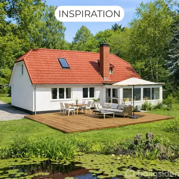Et hvidt hus med rødt tegltag står på en grøn græsplæne. En træterrasse med afslappet møblement er foran huset. Omkranset af træer og en dam med åkander. Tekst: "INSPIRATION".