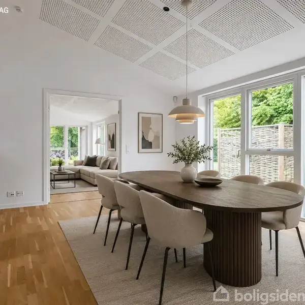 Et elegant spisebord omgivet af otte stole står på et lyst tæppe i en moderne spisestue. Store vinduer til højre giver udsigt til en grøn have. Tekst: "INDRETNINGSFORSLAG".