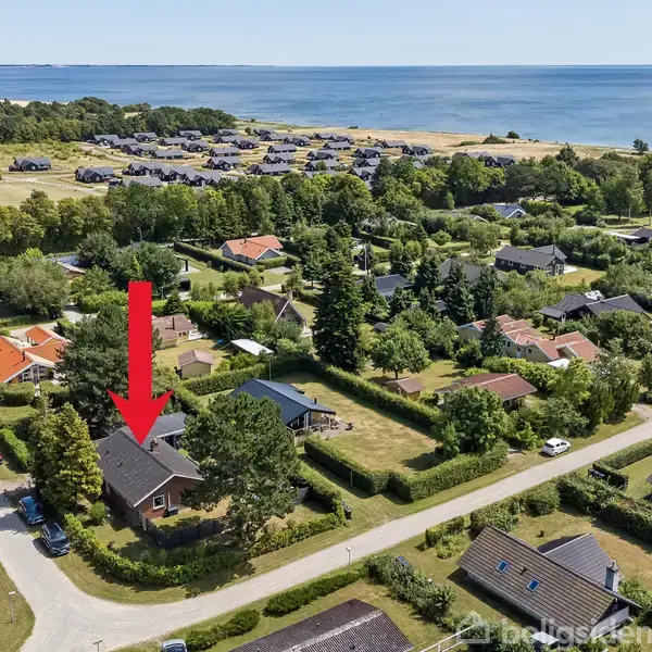 Et rødt murstenshus med græsplæne og terrasse. Terrassen har havemøbler, og en overdækning i baghaven med træer omkring. Himlen er blå med lette skyer.