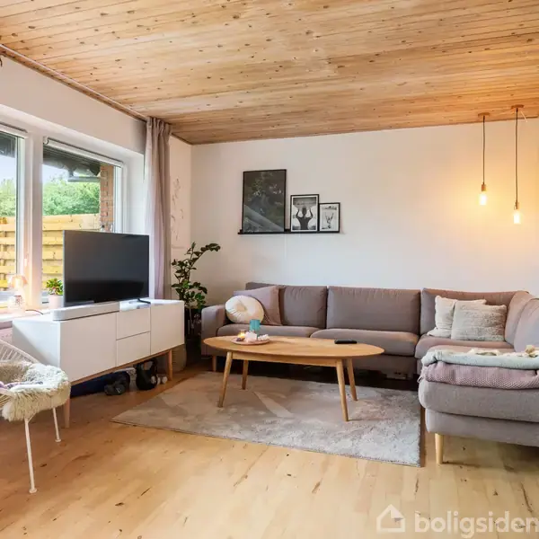 Stue med grå hjørnesofa og træbord på tæppe. Fjernsyn på skænk ved vindue, stol med pude. Hængelamper over sofa, billeder på væggen, lys træloft, grønne planter.