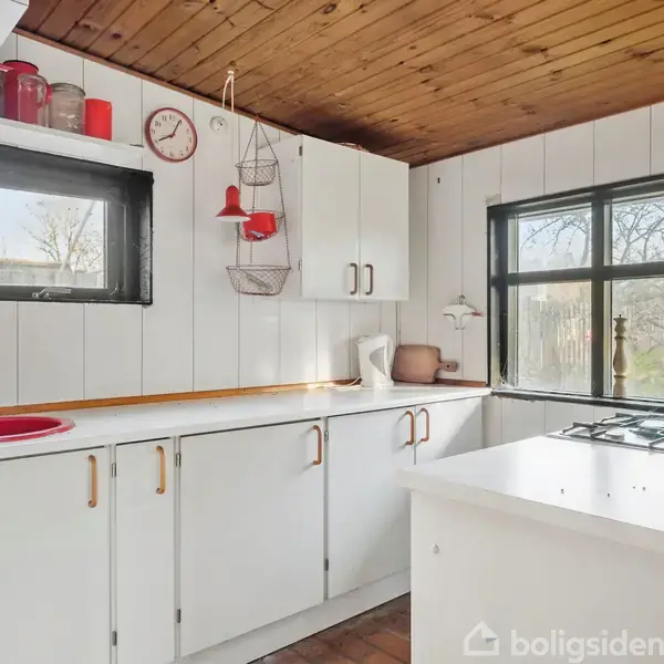 Stue med murstensvægge og trægulv indeholder træmøbler, en brændeovn, en spiseplads og store vinduer, der giver udsigt til en have. En sofa med puder står ved siden af et sidebord.