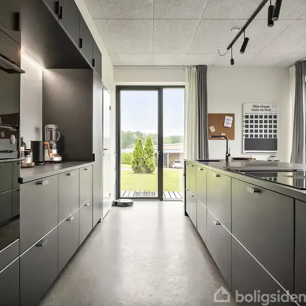 To-etagers moderne hus i mursten med store vinduer og balkon. Det står på en regnvåd terrasse omgivet af grønne græsplæner. Postkassen viser nummer "45B".