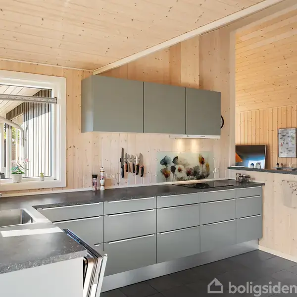 Et moderne køkken med grå skabslåger udfører opbevaringsfunktion. Rummet er lyst med træpaneler på vægge og loft. En stor vindue åbner til en veranda. Bordplader er sorte.