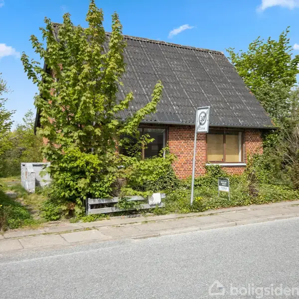En lille, rød murstensbygning med sort tag er delvist skjult af trætter. Skilt foran viser nummer 40. Bygningen grænser op til en vej og er omgivet af grøn vegetation.