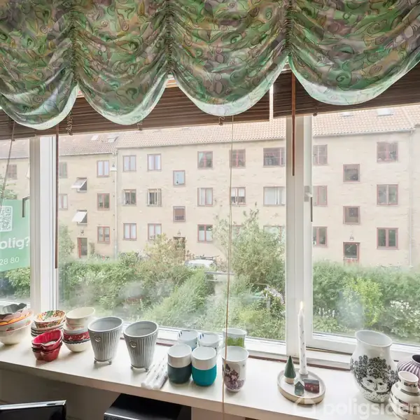 Et vindueskarm med blomstrede gardiner har flere potter, vaser og små dekorative genstande. Udenfor ses et boligkompleks og grønne planter, skaber en fredelig atmosfære. Text: "Find ny bolig? Søg på boligsiden.dk".
