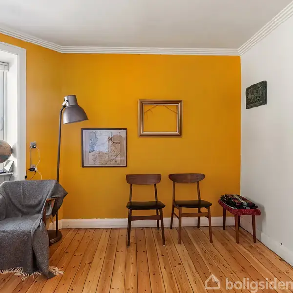 To stole står op ad en gul væg med en lampe ved siden af. Væggen har et kort og en tom ramme. Ved siden af vinduet er et lille bord med en globus.