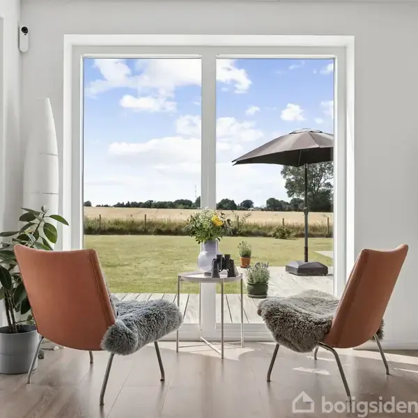 To lænestole med pelsdækken står foran en stor glasdør med udsigt til en have. Mellem stolene er et lille bord med planter, og i baggrunden ses en parasol og en mark.