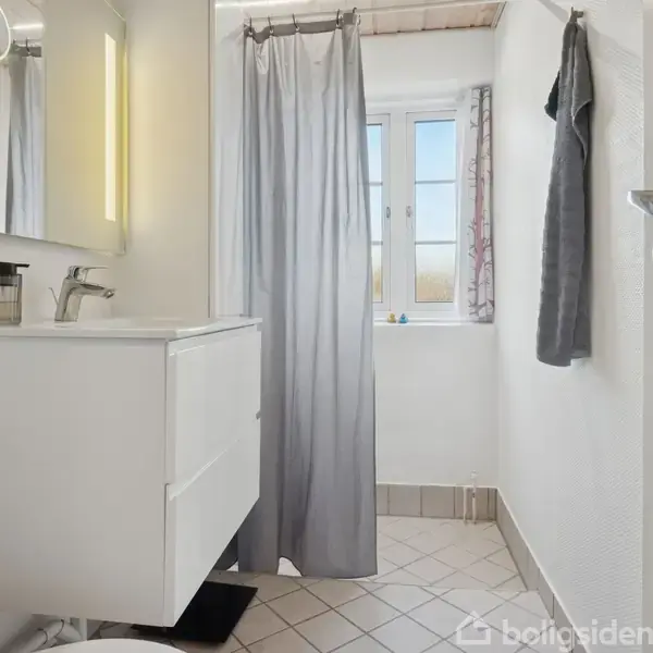 Et hvidt badeværelse med en håndvask og spejl, udfører opgaven at give et sted til personlig pleje; bruseforhæng hænger ved et vindue, som lader naturligt lys strømme ind.