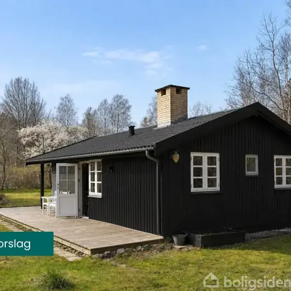 Sort træhus med terrasse står i en grøn have omgivet af træer. Tekst: "Facade forslag".
