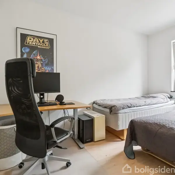 Kontorstol står ved skrivebord med computerskærm og mikrofon; en plakat med teksten "Day of the Tentacle" hænger over skrivebordet. To senge står ved siden af, med udsigt til grøn natur gennem vinduet.