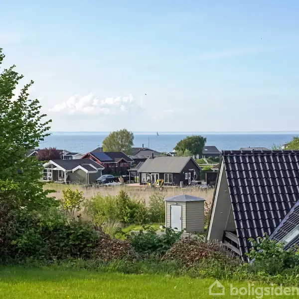 Forskellige huse står i en række, med en have i forgrunden. I baggrunden ses havet og en blå himmel.