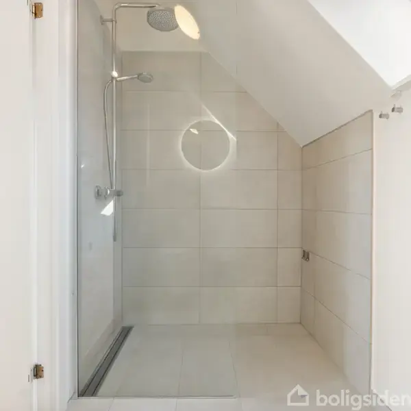 Bruseniche med glasdør, indrettet i et skråt loftsrum med lyst flisegulv og vægge. Der er ingen tekst i billedet.