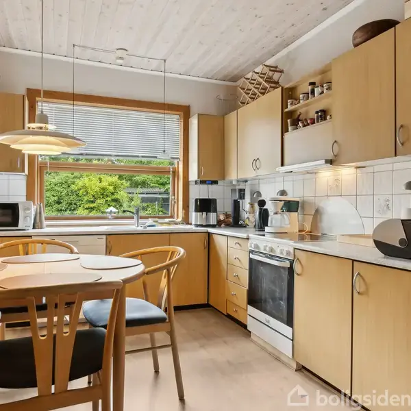 Hvidt hus med rødt tegltag står stille på en gadeflise. Ved siden af ses grusbelagt indkørsel og haveskur. Naboens hus ses i baggrunden.