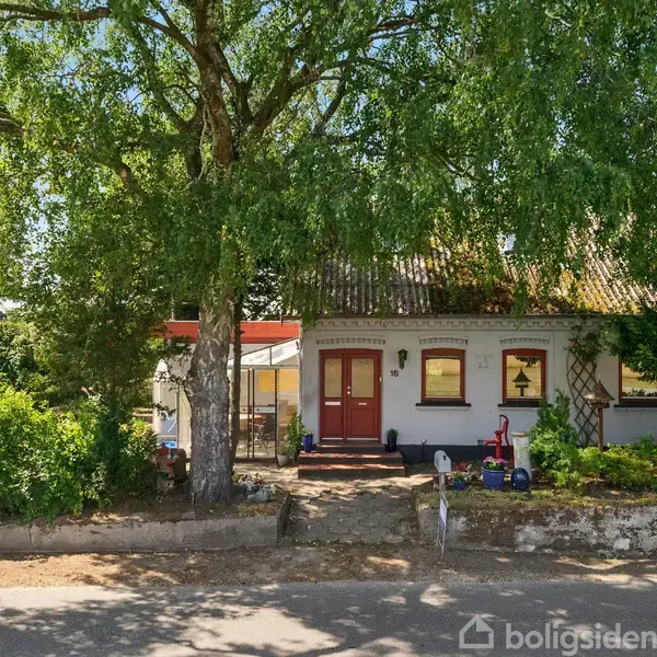 Hus står stille omgivet af frodige træer og buske. Dørmaleri viser nummeret 33 med en postkasse ved siden. Indgangen er flankeret af legetøj og en cykel på terrassen.
