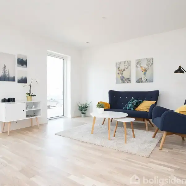 En moderne stue med en blå sofa, to puder og en gul lænestol står på et lyst trægulv. Et hvidt sofabord og en gulvlampesætter rammen. Vægkunst hænger i baggrunden.